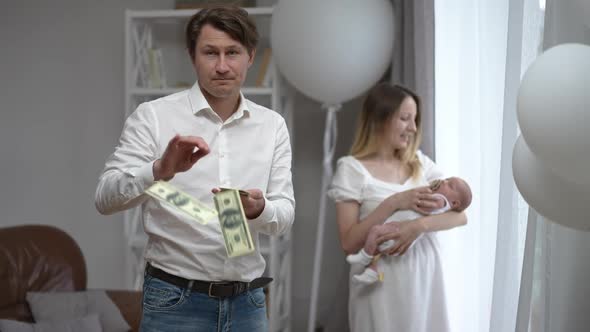 Caucasian Man Scattering Money in Slow Motion with Woman and Newborn Infant Standing at Background