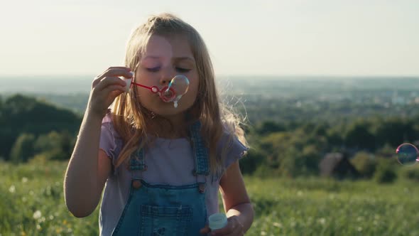 Cute caucasian girl playing with bubbles at the meadow