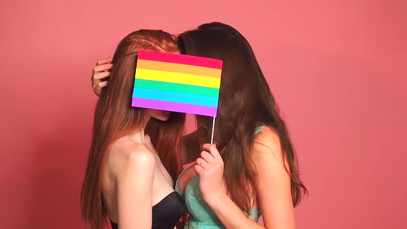 Redhaired Ginger Woman in Pink Studio Background Kissing and Hiding Behind the Rainbow Flag