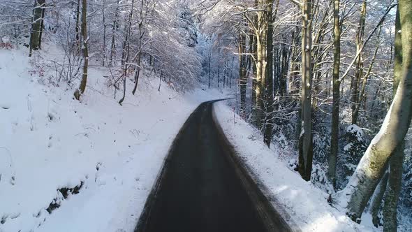 Drone flying low above the road in forest covered with snow