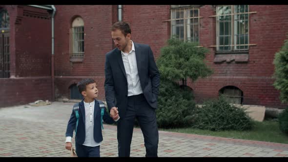 Handsome Guy in Suit and His Child with Backpack Holding Hand in Hand While Walking and Talking