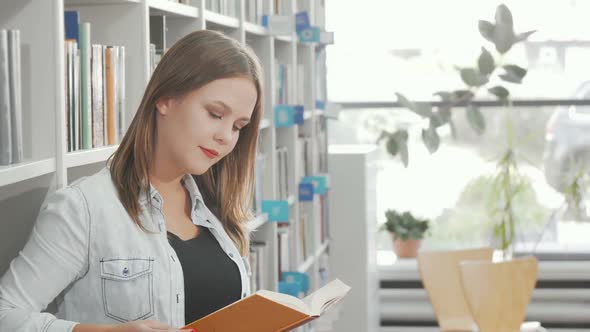 Lovely Young Woman Smiling To the Camera While Reading at the Library