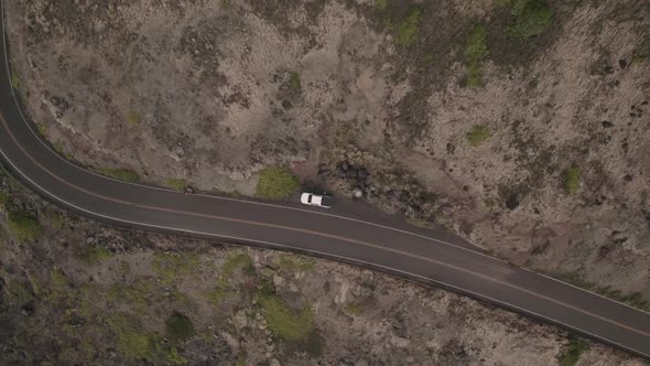 A twisting downward aerial zooming into a parked car on the side of an ancient Hawaiian lava field.