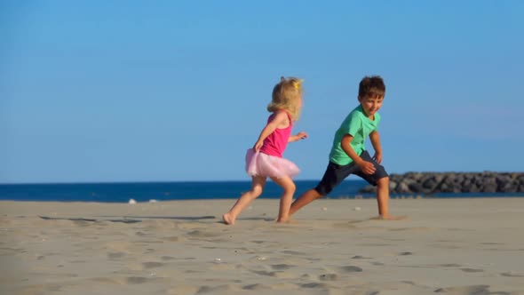 Little Boy and Girl in the Pink Skirt are Playing Catchup on the Beach