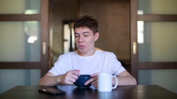Teenager eats porridge and looks at the phone in the morning at breakfast