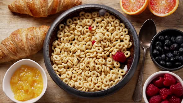 Fresh Berries and Pomegranate Seeds Fall Into the Ceramic Bowl Filled with Cereal Rings