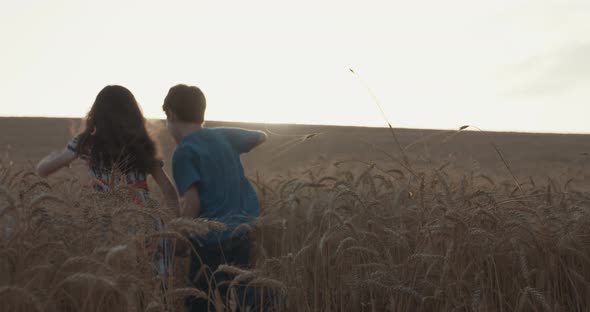 Boy and girl running in a golden wheat field together towards the sunset