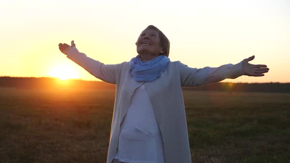 Cheerful Senior Woman With Arms Outstretched To Sunset Sky Standing In Field