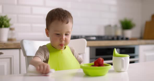 Cute Little Baby Boy Eats Strawberries From Green Plate and Wipes Table with Rag