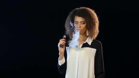 Girl of African American Appearance Smokes an E-cigarette, Black Background