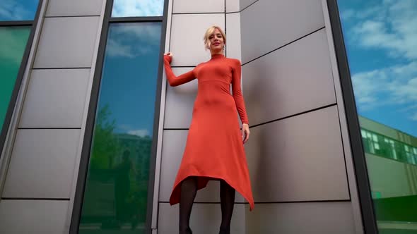 a Blonde in a Red Dress Poses Near Large Green Windows. the Camera Moves From Bottom To Top