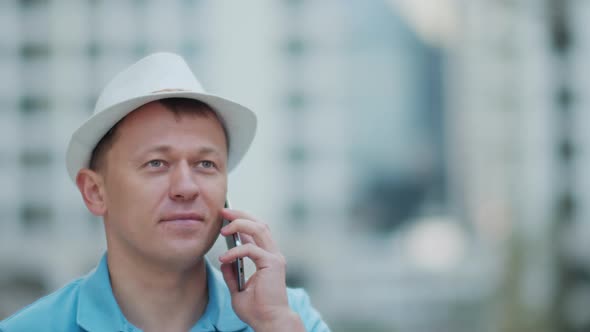 Man in a white hat talking on a mobile phone while standing on a city street tracking camera