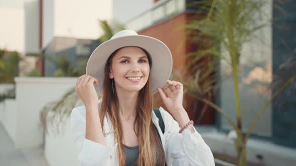 Positive Young Woman in Stylish Clothes and White Hat Smiling Sincerely on