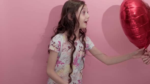 Beautiful Girl on a Pink Background with a Red Balloon in the Shape of a Heart