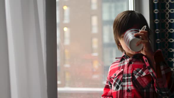 Boy Child in a Plaid Shirt is Sitting By the Window and Drinking Tea