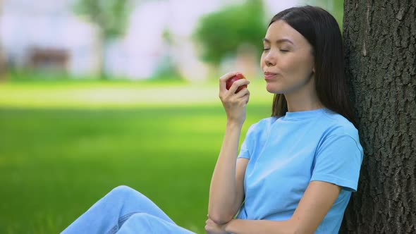 Asian Female Eating Fresh Apple Sitting Outdoors