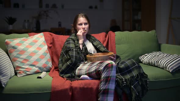 Sleepy young woman watching tv at night and eating chips