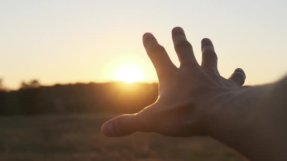 Male Hand Against Sunset. Touch the Sun. Sun Shines Through Fingers. Slow Motion