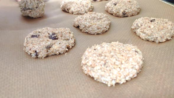 Raw biscuits on a baking tray with brown baking paper are in shot. A blump of cookie dough is place