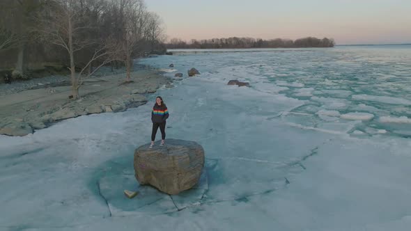 young women wearing pride colors jacket on a Rock in the middle of a frozen lake