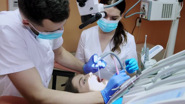 Dentist with assistant under microscope treats the patient's teeth. Modern progressive dentistry.