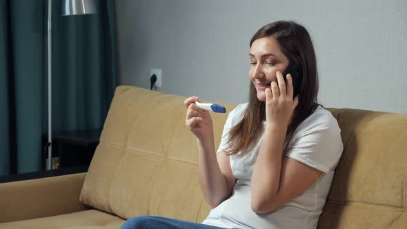 Happy Woman Talking on the Phone Holding Pregnancy Test in Hands