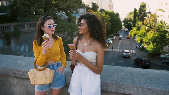 Two Young Smart Dressed Women in Sunglasses are Eating Icecream Talking and Laughing While Posing on