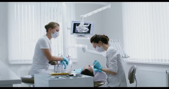 A Female Dentist Examines the Oral Cavity of a Patient Lying on a Dental Chair