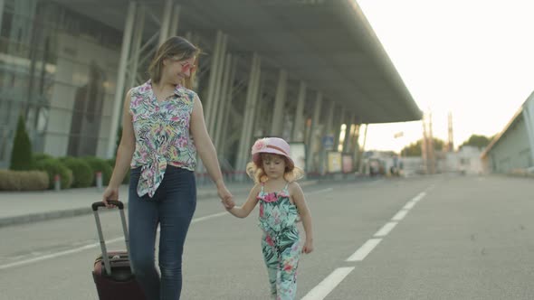 Mother and Daughter Walking From Airport. Woman Carrying Suitcase Bag. Child and Mom After Vacation