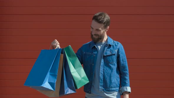 Happy Modern Man Holding Shopping Bags and a Credit Card with a Toothy Smile, Looking at the Camera