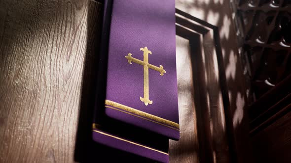 Purple stole with cross lightened by rays of light falling into a confessional.