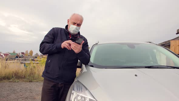 Business Man in a Medical Mask Standing By the Car Works Online on a Smartphone