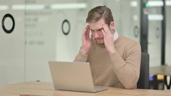 Creative Young Man with Laptop Having Headache in Office