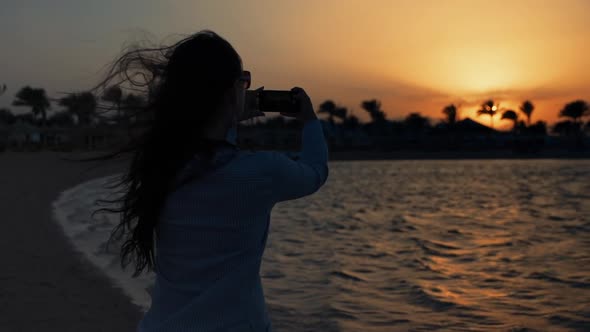 Attractive Woman Taking Picture of Sunset Sea on Mobile Phone at Seaside.