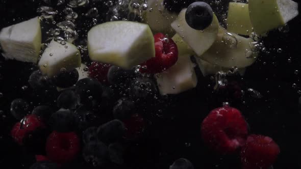 Raspberries, Blueberries, Blackberries and Apple Pieces Fall Into the Water on a Black Background