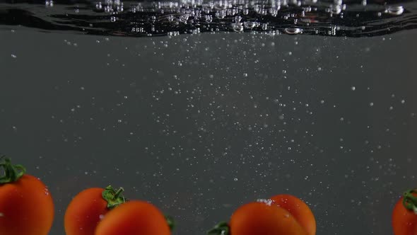 Closeup of Fresh and Health Cherry Tomatoes Falling Into Clear Water with Big Splash on Black