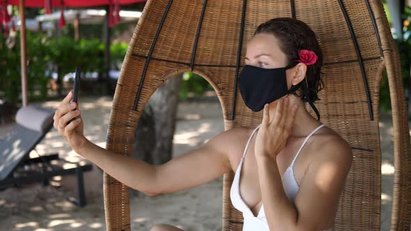 Young Female Blogger in a Face Mask Looking for the Best Angle to Take a Selfie in a Cocoon Chair on