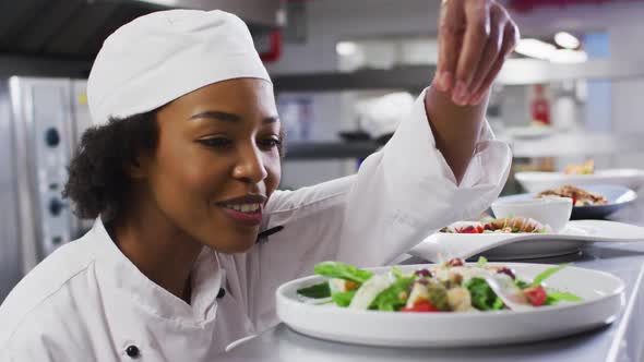 African american female chef garnishing dish and similing in restaurant kitchen