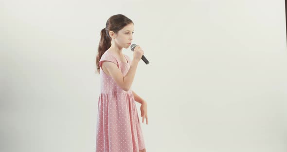 young girl sings into a microphone on a white studio background