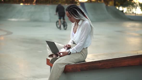 Side View of Beautiful Elegant Girl with Black and White Dreadlocks Sitting on Parapet in Local