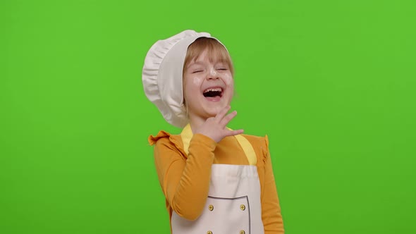 Child Girl Dressed Cook Chef Baker in Apron and Hat Laughing Out Loud After Hearing Funny Joke