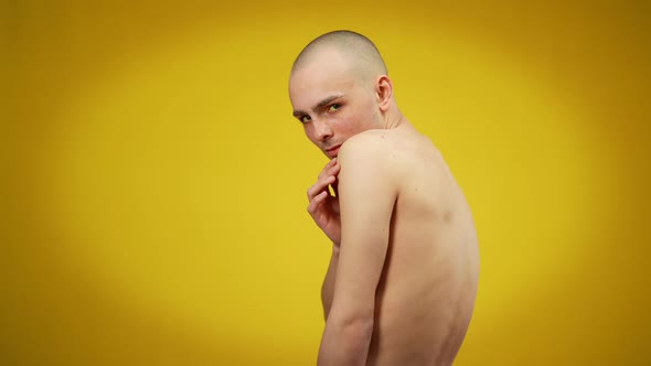 Side View Medium Shot of Young Caucasian Male Queer Looking at Camera Posing at Yellow Background