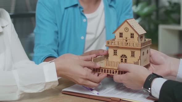 Close Up Of A Couple's Hands Receiving A House Model From A Real Estate Agent After Signing