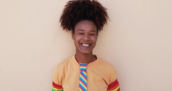 African lesbian woman wearing rainbow accessoires while smiling on camera - LGBT and homosexual love