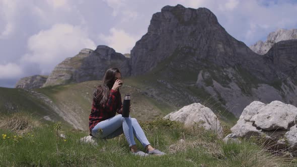 Female Traveler Drinking Tea In Thermos Mug In Mountains