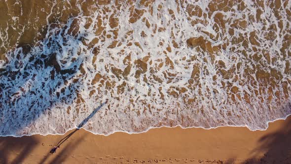 Waves rolling ashore. Woman walks on the beach. Top view (aerial), background.