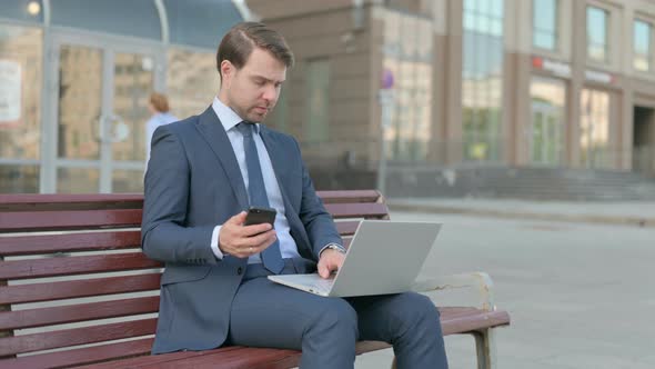 Businessman Using Smartphone and Laptop while Sitting Outdoor on Bench