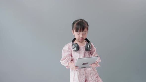 Girl with dress dancing and spinning with headphones in front of gray background.