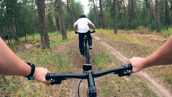 Two Riders Are Cycling Along the Forest Trail