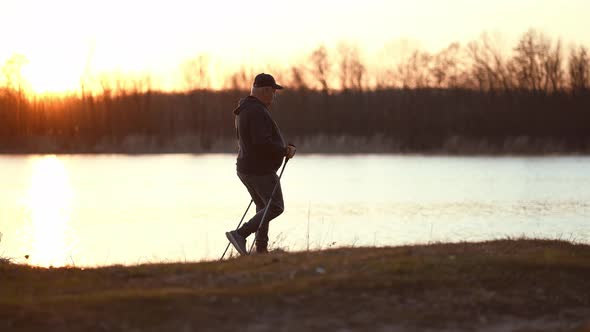 Side View a Man Sport Fitness Nordic Walking with Special Stick on the Ground Next to Water